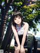 A girl in a school uniform crouching down next to a trash can.