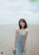 A woman standing on a beach in a blue dress.