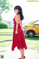 A woman in a red dress standing in front of a yellow car.