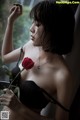 A woman in a black bra holding a red rose.