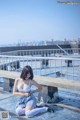 A woman sitting on a concrete bench near the water.