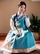 A woman in a blue and white hanbok sitting on the floor.