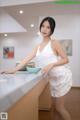 A woman in a white dress standing in a kitchen.