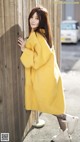 A woman leaning against a wooden fence wearing a yellow coat.